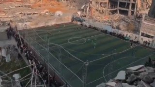 На износено игрище за футбол с пет играча сред разрушени